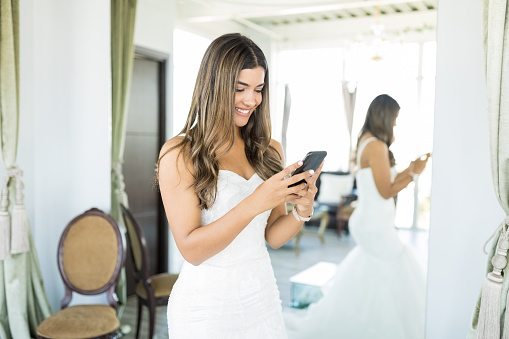 Hispanic customer smiling while using application on mobile phone in bridal studio