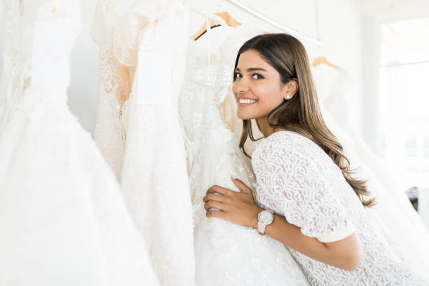 Woman Buying Beautiful Marriage Gown In Store Good looking woman smiling while selecting white wedding dress at boutique bridal shop photos stock pictures, royalty-free photos & images