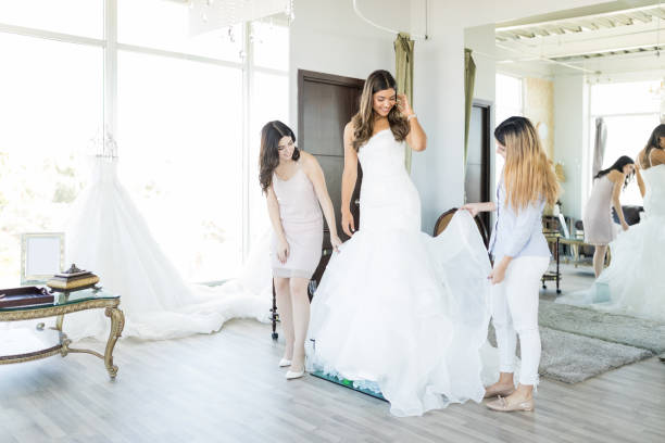Women Admiring White Wedding Gown In Store Female customers checking out dress worn by beautiful friend in bridal shop bridal shop photos stock pictures, royalty-free photos & images