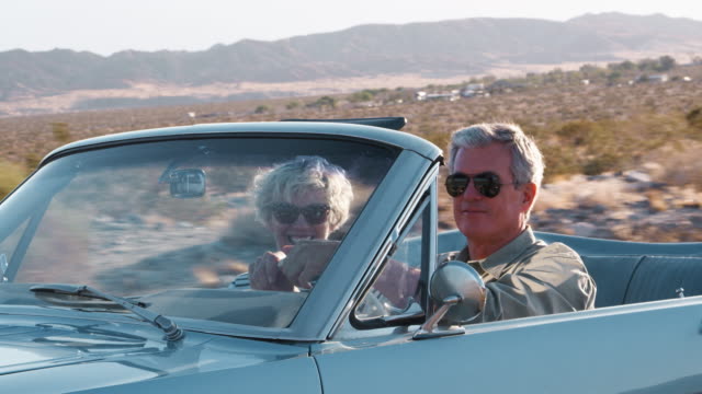 Senior couple driving in open top car on a desert highway