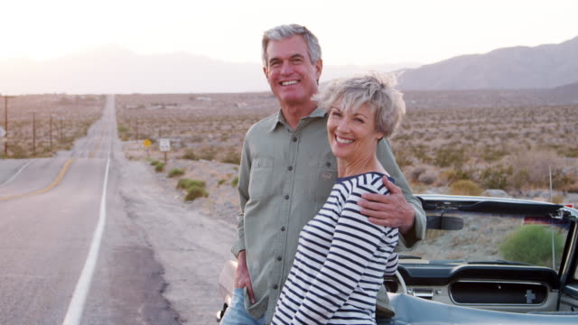 Senior couple standing by car smiling to camera, close up
