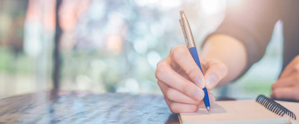 mano de mujer escribiendo en un bloc de notas con un bolígrafo en la oficina - diary writing women human hand fotografías e imágenes de stock