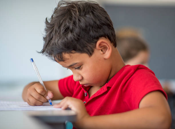 istock Cute boy writing on paper in school 1071267798