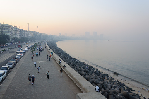 Mumbai, India. December 25, 2011. \nCitizens of South Mumbai, India taking an early morning walk, exercising, jogging or enjoying fresh air at Marine Drive with skyscrapers and towers at Nariman Point visible through haze in the background.