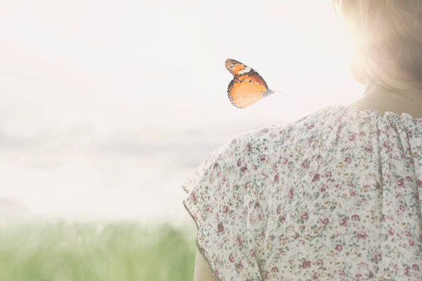 a colorful butterfly leans delicately on the shoulders of a girl stock photo