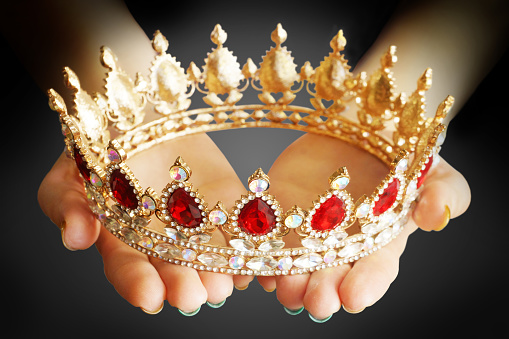 Woman's hands holding golden crown with red and white diamonds against black background