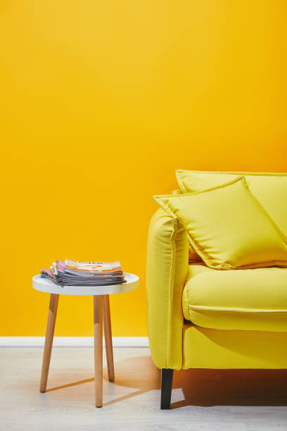 istock Sofa with pillows and little table with journals near yellow wall 1071308778