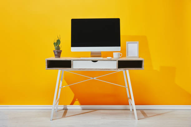 istock Computer, photo frame, cup of coffee and cactus at workplace near yellow wall 1071308872