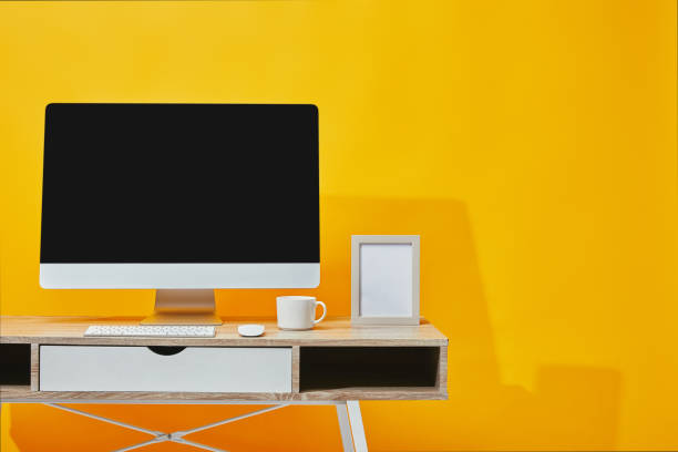 istock Computer, cup of coffee and photo frame at wooden table on yellow 1071308888