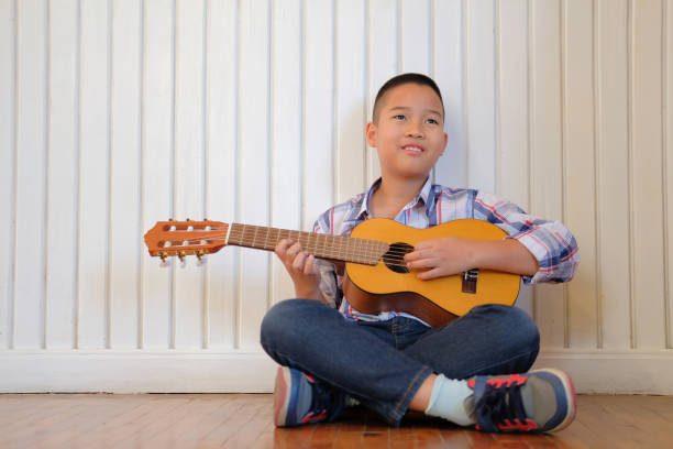 istock asian kid boy child playing guitar ukulele. children leisure activity 1071310918