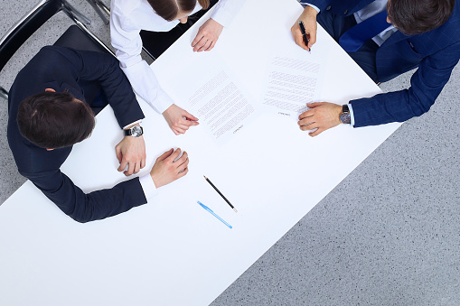 Group of business people and lawyer discussing contract papers sitting at the table, view from above. Businessman is signing document after agreement done.