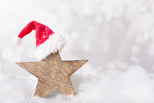 star made of wood with red Christmas cap in the snow, white bokeh background, text space