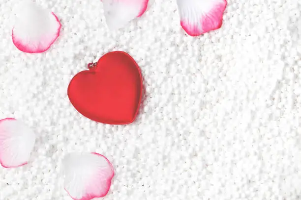 Valentines Day background concepts. Red heart and petals of roses lies on white balls, close up. Top view. Copy space