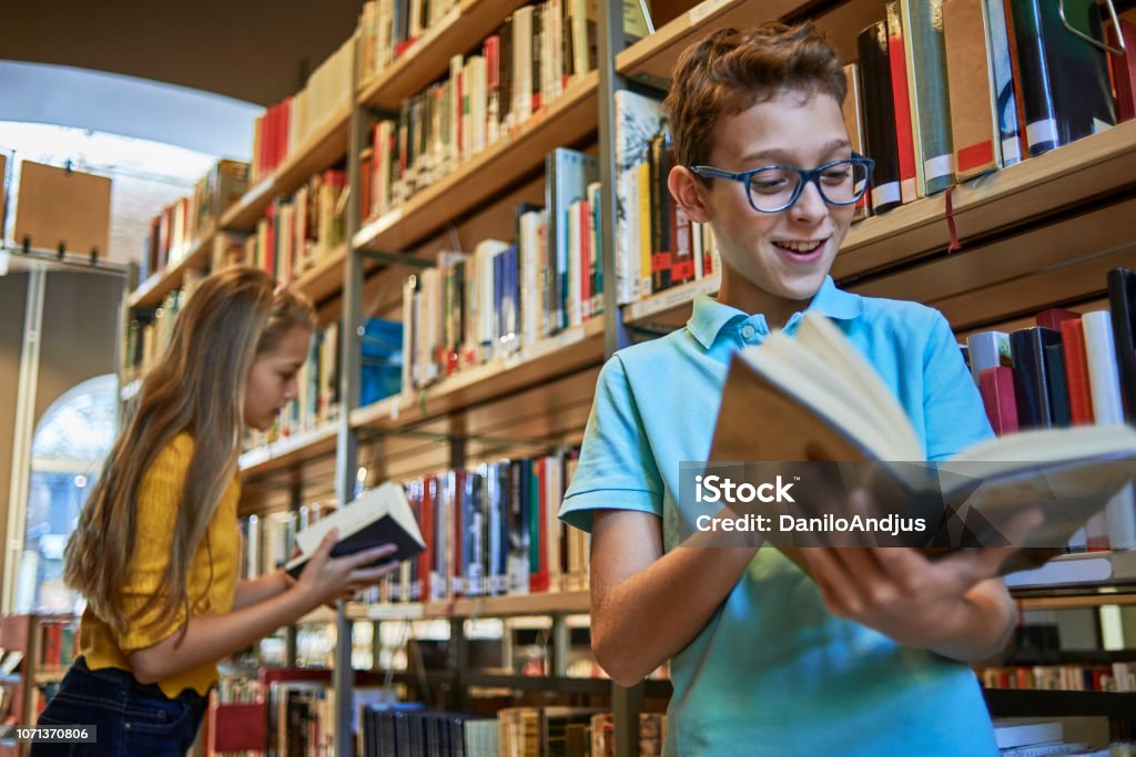 school boy reading a book in the library young student reading a book in the library Library Stock Photo