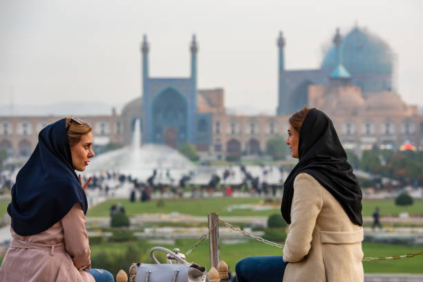 Iranian women in front of Shah Mosque, Isfahan Isfahan, Iran - November 19, 2018: Two Iranian women are sitting on a terrace in front of the famous Shah Mosque on Imam Square, Isfahan, Iran. The mosque is also known as Imam Mosque and Jaame' Abbasi Mosque. It is one of the masterpieces of Iranian/Persian Architecture and an excellent example of Islamic era architecture of Iran and also one of the top sights of the country. isfahan stock pictures, royalty-free photos & images