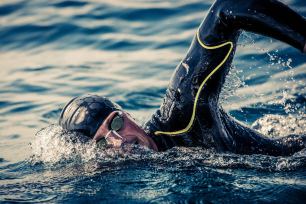 Open water swimmer swimming in sea Male open water swimmer swimming forward crawl in sea. neoprene photos stock pictures, royalty-free photos & images