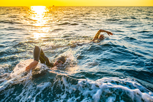 Man and woman swimming forward crawl at sea in sunshine.