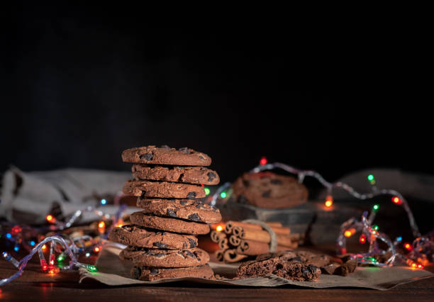 round chocolate cookies in a stack, around the New Year's burning garlands on a brown table