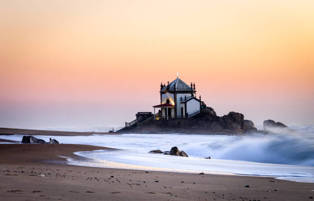 Side view of Senhor da Pedra Chapel at sunset with waves crashing in the sand. Golden hour. Copy Space.