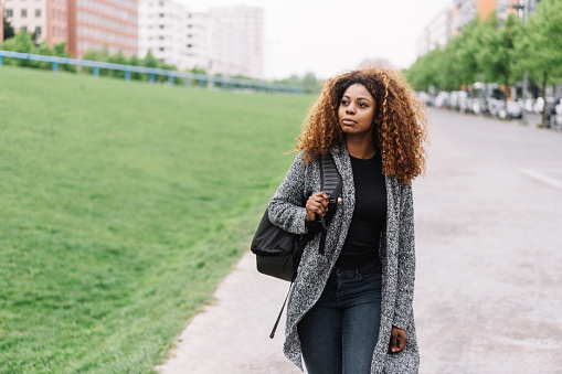 Portrait of young black woman with curly hair walking along street