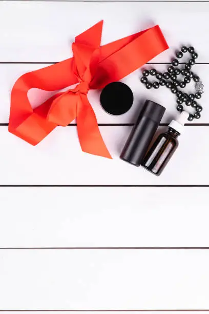 black colour beauty products, black pearls, red ribbon, hair brush on a white wooden backdrop