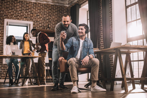 istock two men using smartphone with multiethnic group of casual businesspeople working in modern loft office behind 1071388624