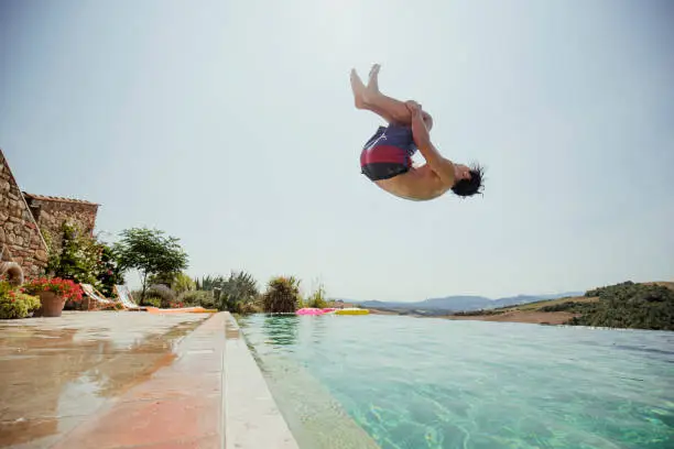 One young man performing a backflip into an outdoor swimming pool at a holiday villa in Tuscany, Italy.
