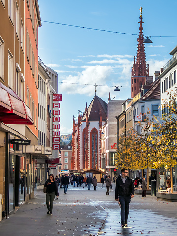 Würzburg, Germany - November 11, 2018: Pedestrians walk through the Eichhornstraße in Würzburg. In the background is the famous Mareinkirche.