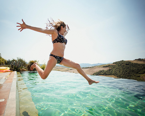 Mature woman jumping into the pool on holiday.