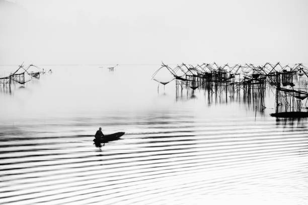 black and white silhouette scenery of fisherman on boat and traditional fish trap at Parkpra, Patthalung, Thailand black and white silhouette scenery of fisherman on boat and traditional fish trap at Parkpra, Patthalung, Thailand phatthalung province stock pictures, royalty-free photos & images