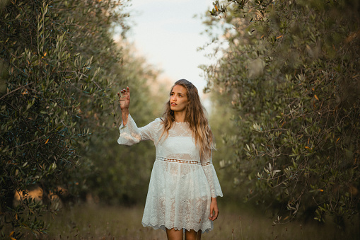 Young, beautiful female standing in a field looking up towards the plants growing around her.