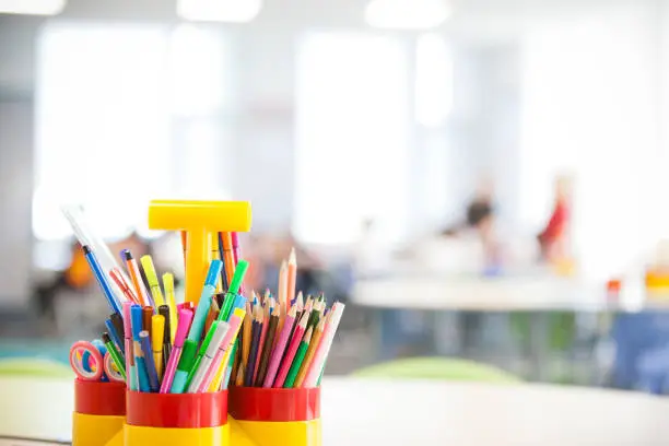 Close-up selective focus of color pencils and pens in holder in classroom.