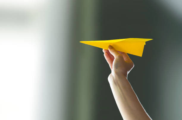 Hand holding paper airplane Woman hand holding a yellow paper airplane paper airplane photos stock pictures, royalty-free photos & images