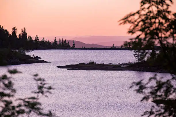 Lake surrounded with forest, rocks and mountains. Beautiful view of pink sky, landscape in dusk. Norway, Kongsberg