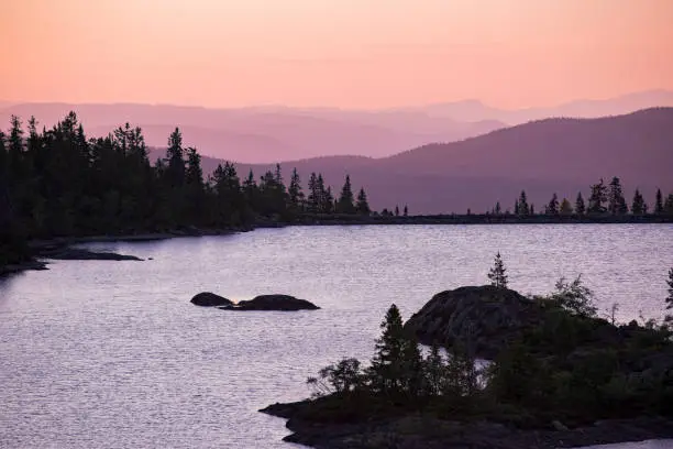 Lake surrounded with forest, rocks and mountains. Beautiful view of pink sky, landscape in dusk. Norway, Kongsberg