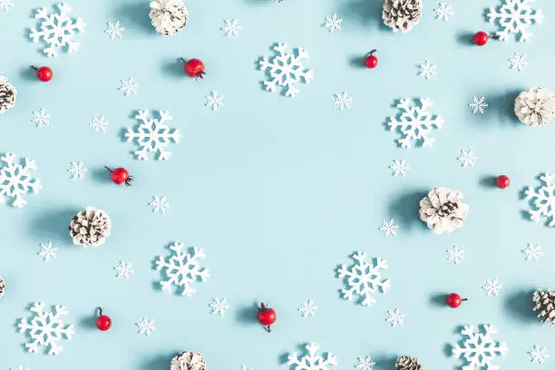 Christmas or winter composition. Frame made of snowflakes, pine cones and red berries on pastel blue background. Christmas, winter, new year concept. Flat lay, top view, copy space