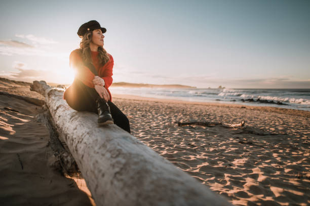 istock Young woman sitting by a beach at sunset in winter 1071437030