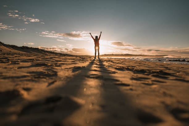 A person strolls peacefully on the sandy beach during sunset, basking in the warm glow of the sun as it reflects on the water and creates a serene atmosphere.