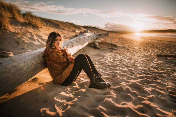 mujer joven sentada junto a una playa al atardecer en invierno - beach beauty in nature beautiful brown hair fotografías e imágenes de stock