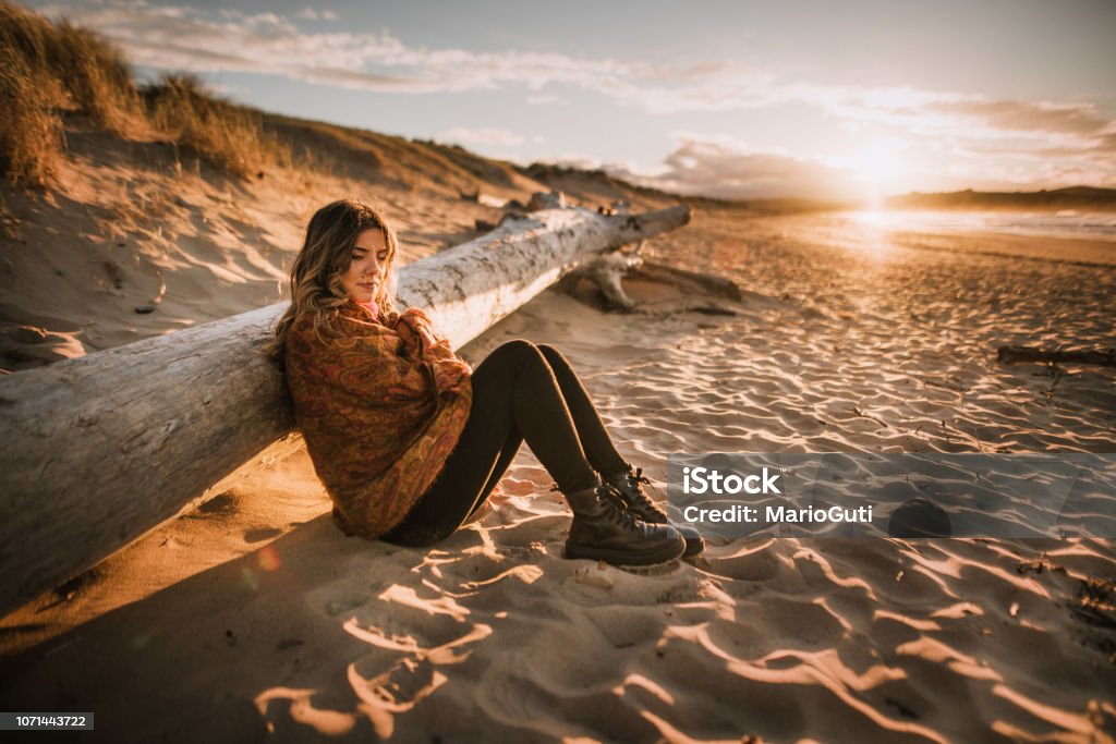 Jonge vrouw zitten door een strand bij zonsondergang in de winter - Royalty-free Strand Stockfoto