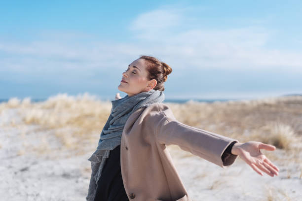 Happy carefree young woman on a winter beach Happy carefree young woman on a winter beach enjoying the warm sunshine with outspread arms and closed eyes breath vapor stock pictures, royalty-free photos & images