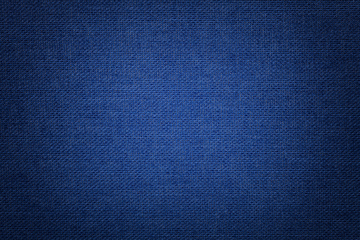 Dark azure background from a textile material with wicker pattern, closeup. Structure of the navy blue fabric with texture. Cloth denim backdrop with vignette.