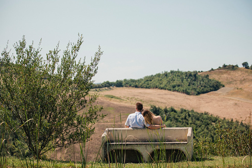 Young couple sitting on a bench admiring the beautiful view in Tuscany.