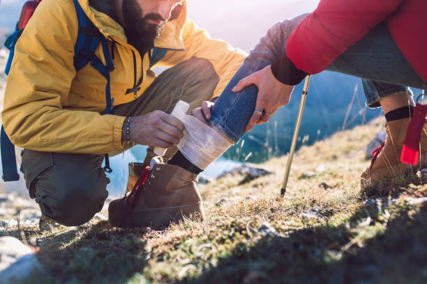A woman has sprained her ankle while hiking, her friend uses the first aid kit to tend to the injury A woman has sprained her ankle while hiking, her friend uses the first aid kit to tend to the injury first aid photos stock pictures, royalty-free photos & images