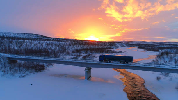 antenne : camion semi traverser le pont au-dessus de la rivière glaciale en hiver au coucher du soleil - winter sunset sunrise forest photos et images de collection