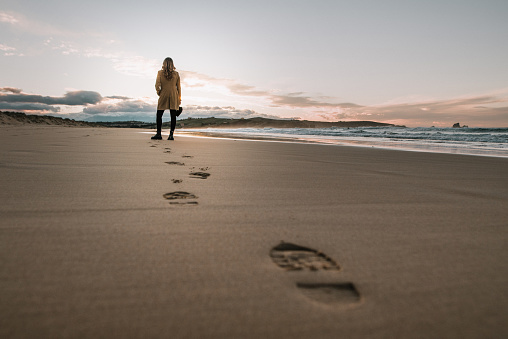 Young woman walking over a beach and leaving her footprints on the sand