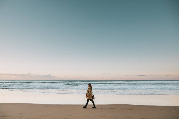 vista lateral de la joven mujer caminando por la playa al atardecer - beach beauty in nature beautiful brown hair fotografías e imágenes de stock
