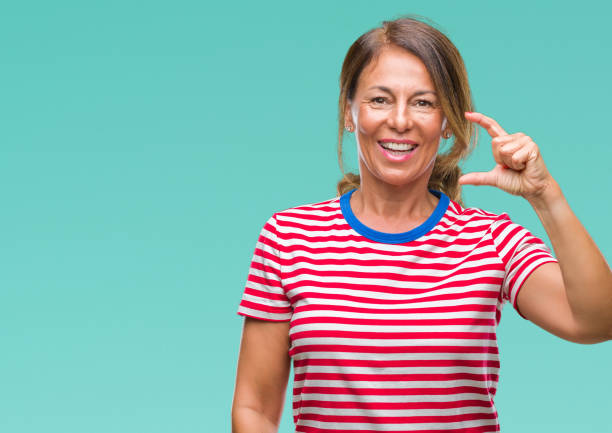 istock Middle age senior hispanic woman over isolated background smiling and confident gesturing with hand doing size sign with fingers while looking and the camera. Measure concept. 1071462034