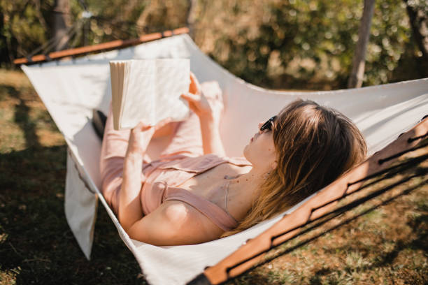 Enjoying the Summer Young female adult relaxing outside during the summer. She is lying on a hammock enjoying the peace and quiet in Tuscany. hammock relaxation women front or back yard stock pictures, royalty-free photos & images