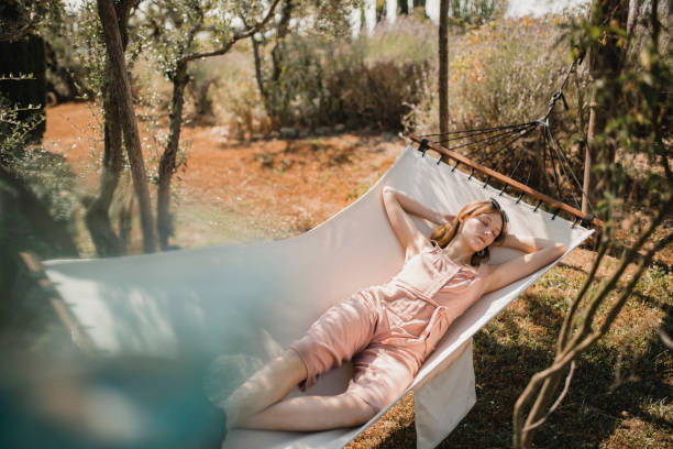 Relaxing in a Hammock Young female adult relaxing outside during the summer. She is lying on a hammock enjoying the peace and quiet in Tuscany. hammock relaxation women front or back yard stock pictures, royalty-free photos & images